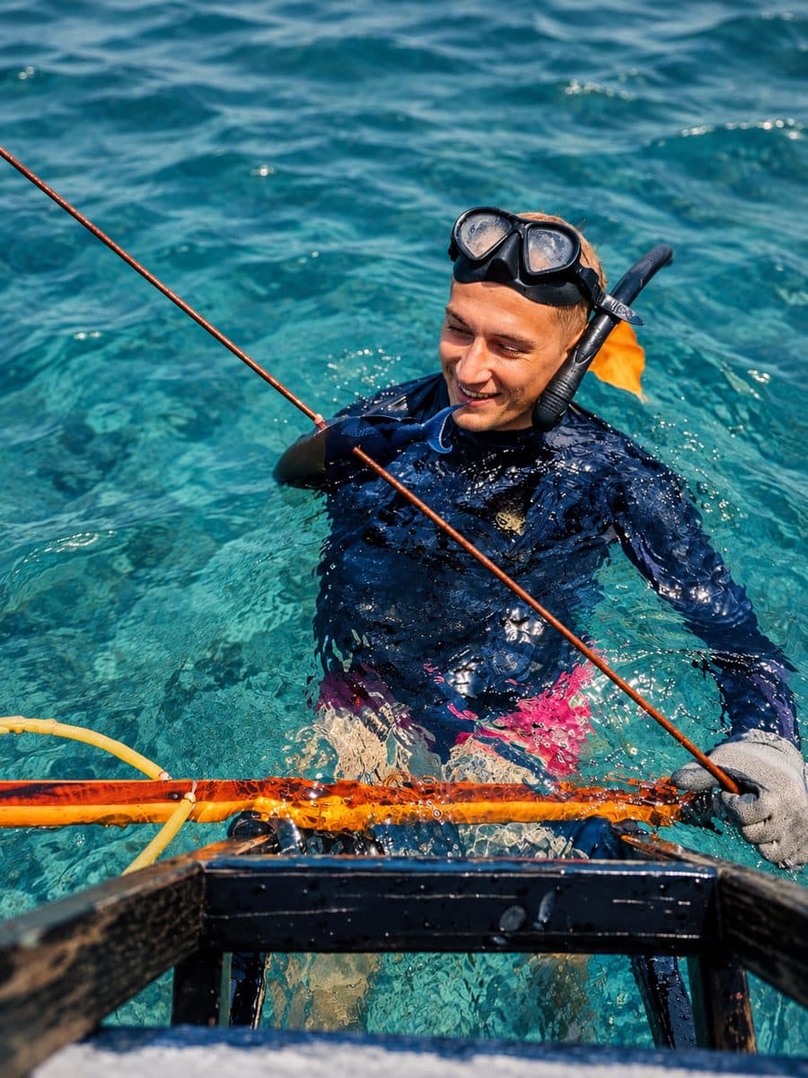 Smiling in turquoise water after a dive, holding the boat's line.